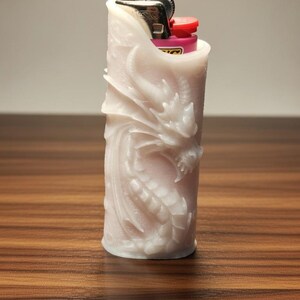 May include: A white, cylindrical lighter cover with a detailed dragon carving. The lighter cover is made of a solid material and has a red and black lighter visible at the top. The background is a wooden surface.