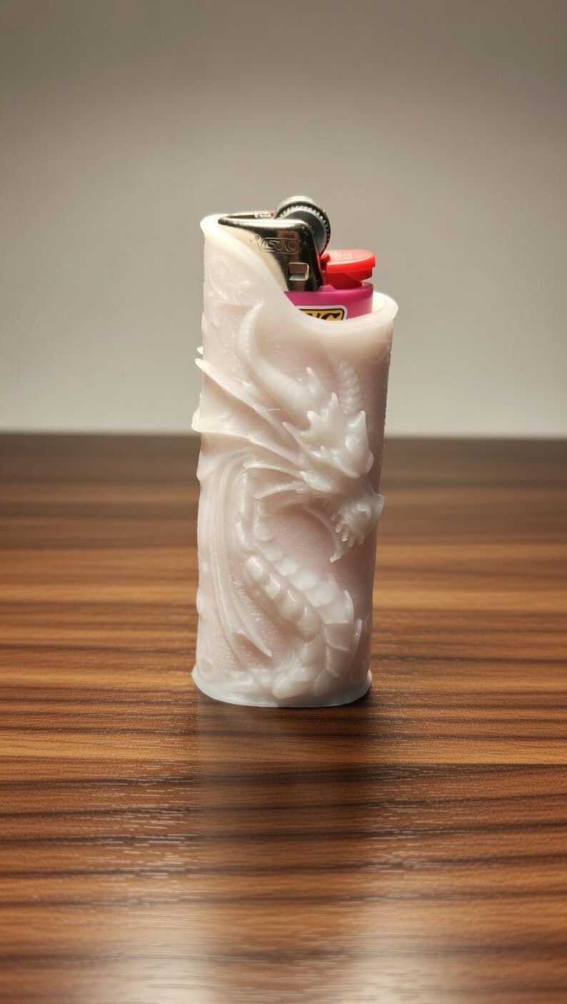 May include: A white, cylindrical lighter cover with a detailed dragon carving. The lighter cover is made of a solid material and has a red and black lighter visible at the top. The background is a wooden surface.