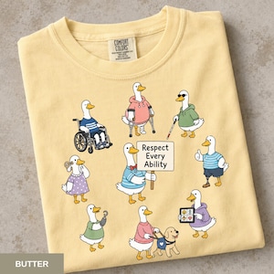 May include: A butter yellow t-shirt featuring a graphic of eight cartoon ducks with various disabilities and assistive devices. One duck holds a sign that reads Respect Every Ability. The shirt has a Comfort Colors brand label at the neck.
