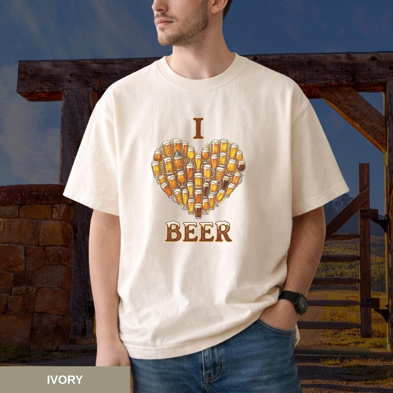 May include: Cream-coloured t-shirt featuring a heart made of beer glasses. The word "I" is above the heart, and "BEER" is below it in brown letters. The shirt is a casual style.