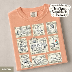 May include: A peachy-orange t-shirt featuring a grid of nine postage stamp-style illustrations related to ADHD support. The graphics include labels like ADHD Planning Tool, Executive Function, Focus, Sensory Integration Aid, and ADHD Support Services.
