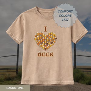 May include: A sandstone-coloured t-shirt featuring a heart composed of beer glasses. The word "I" is above the heart, and "BEER" is below. The shirt has short sleeves and a crew neck. The Comfort Colors 1717 tag is visible.