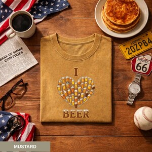 May include: Mustard-coloured t-shirt with a heart-shaped design made of beer mugs and the words "I BEER". The image includes a baseball, watch, pancakes, and an American flag.