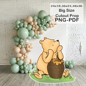 Op de afbeelding: Een Winnie de Poeh-uitgesneden prop met een honingpot, tegen een ballonnenboog in pastelkleuren. De tekst op de afbeelding luidt "Big Size Cutout Prop PNG-PDF" en vermeldt de maten 61x46, 91x61 en 122x91 cm.