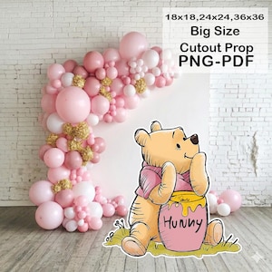 Op de afbeelding: Een grote kartonnen prop met Winnie de Poeh en een honingpot, tegen een achtergrond van roze en witte ballonnen. De tekst op de prop luidt "Big Size Cutout Prop PNG-PDF" en de afmetingen zijn 45x45, 61x61 en 91x91 cm.