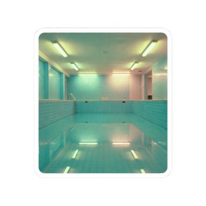 May include: An empty indoor swimming pool with turquoise tiles and a ladder. The pool is rectangular, with the water reflecting the fluorescent lights on the ceiling. The walls are tiled in a matching turquoise color, creating a serene, minimalist aesthetic.