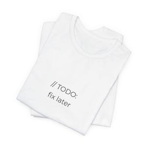 Könnte beinhalten: Zwei weiße T-Shirts übereinander gestapelt. Das obere T-Shirt hat den schwarzen Text "// TODO: fix later" aufgedruckt. Die Shirts bestehen aus weichem Material und sind ordentlich gefaltet.