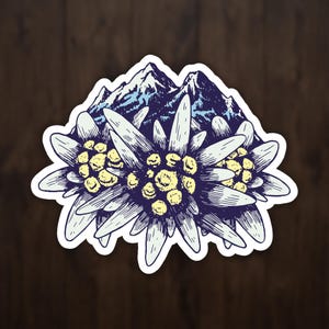 Puede incluir: Una pegatina con una ilustración estilizada de flores de edelweiss y una cordillera en el fondo. Las flores son blancas con centros amarillos, y las montañas son azules y blancas. La pegatina tiene un borde blanco.