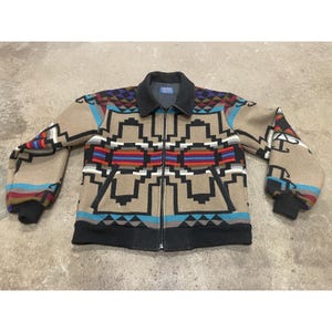 Può includere: Giacca beige con zip e motivo geometrico nero, rosso, blu e viola. La giacca ha colletto e polsini neri. La giacca è lunga circa 71 cm.