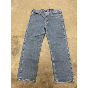 May include: Light blue denim jeans with a classic five-pocket design. The jeans have a straight leg cut and a button and zipper closure. The stitching is a contrasting light brown color.