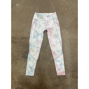 May include: White athletic leggings with a colourful tie-dye pattern in shades of pink, blue, and green. The leggings have a high waist and light blue stitching details. A stylish choice for workouts or casual wear.