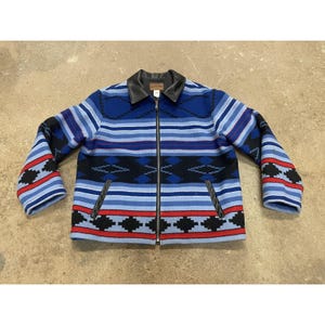 Puede incluir: Chaqueta estampada en azul, rojo y negro con cuello de cuero negro y cierre de cremallera. La chaqueta presenta un diseño geométrico con rayas horizontales y formas de diamante. Las mangas tienen un patrón rojo y negro.