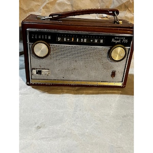 May include: A vintage Zenith Deluxe Royal 755 portable radio featuring a brown leather-like casing, a silver metal speaker grille, two circular control knobs, and a top carrying handle. The black radio dial displays frequency numbers.