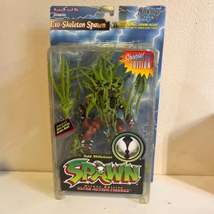 May include: Exo-Skeleton Spawn action figure in a plastic package. The figure is a Special Edition, with green and brown coloring. The packaging includes the text "America's Best Selling Comic Book" and "Deluxe Edition Ultra-Action Figures."