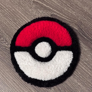 May include: A round, handmade rug featuring a red and white design with a black border. The rug's design resembles a Pokeball, a popular item from the Pokemon franchise. The rug is made of a soft, textured material.
