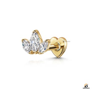 以下が含まれることがあります： マーキス型のキュービックジルコニアのクラスターデザインのゴールドイヤリング。イヤリングは、3つの透明で輝く石とハート型の裏地が特徴です。シングルイヤーピアス用に設計されています。