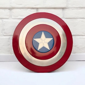 May include: A round shield with a red outer ring, a silver middle ring, and a blue center. A white star is in the center of the blue circle. The shield is a popular superhero accessory.