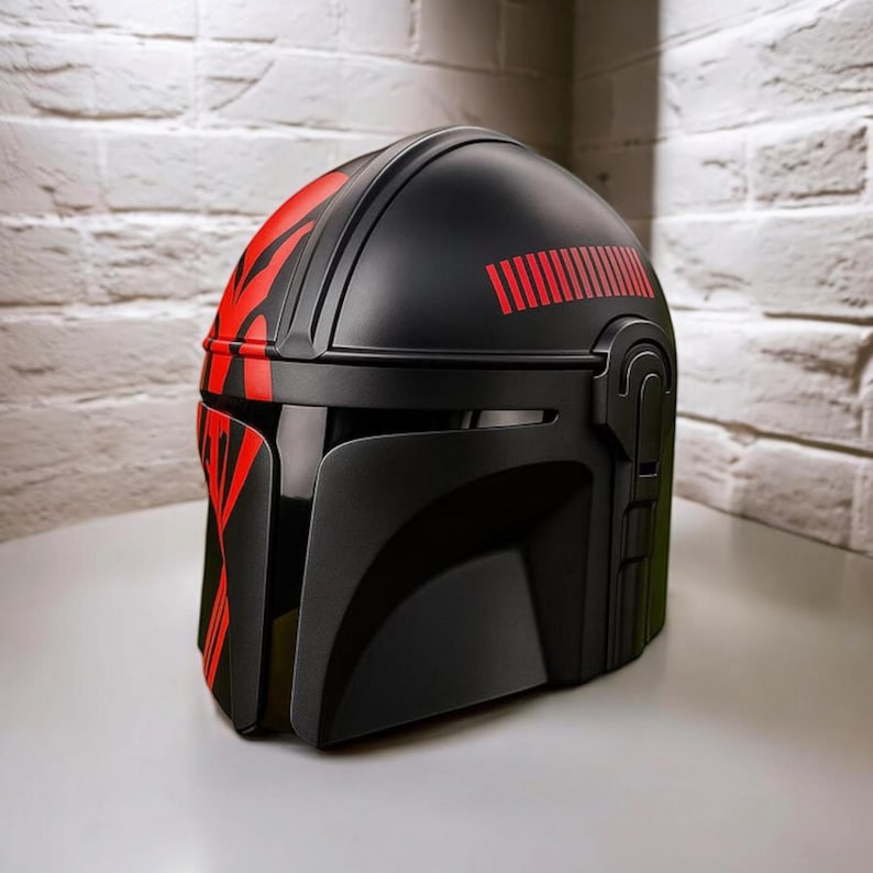 May include: Black helmet with red detailing, including a visor and a curved top. The helmet has red stripes on the side and a series of red lines across the top. The design is reminiscent of a sci-fi or fantasy theme.