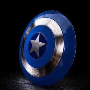 Op de afbeelding: Een blauw en zilver schild met een centrale zilveren ster. Het schild heeft een cirkelvormig ontwerp met concentrische ringen van blauw en zilver. Het is een rekwisiet of verzamelobject.