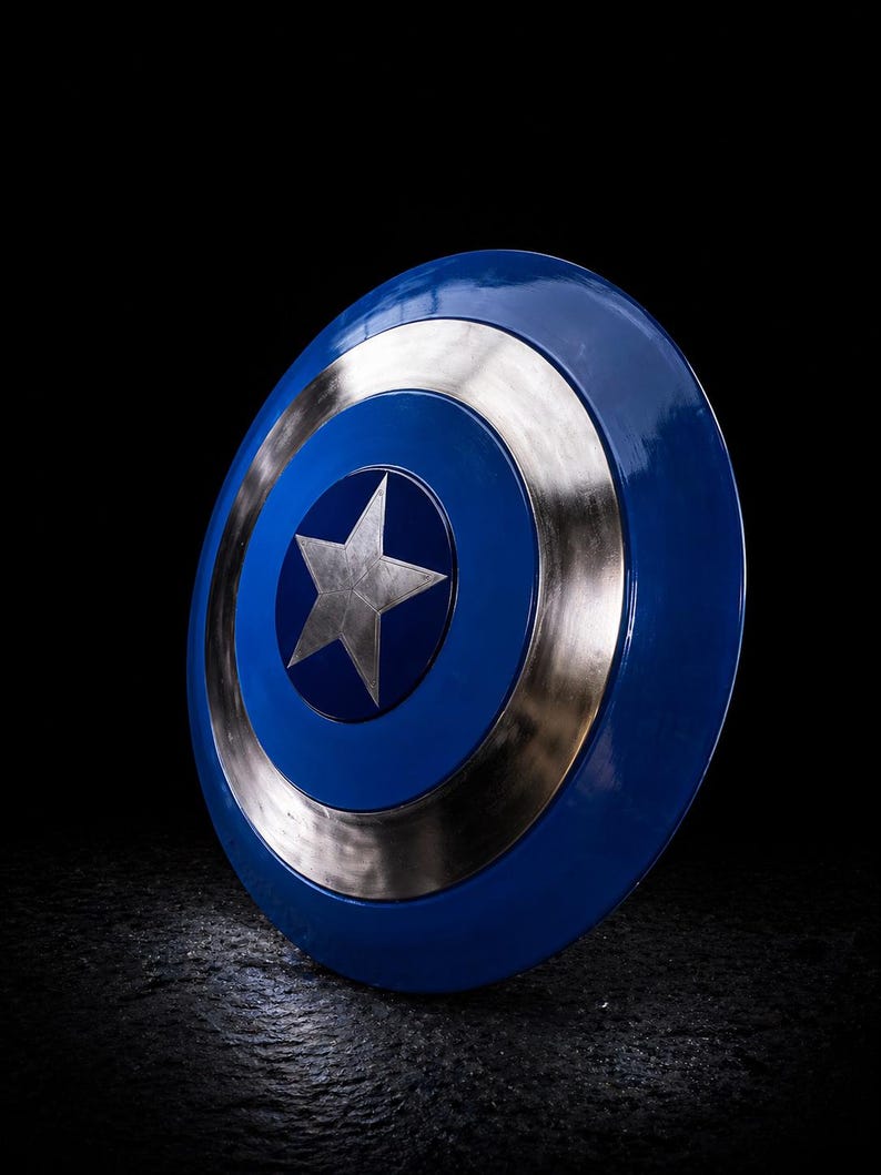 Op de afbeelding: Een blauw en zilver schild met een centrale zilveren ster. Het schild heeft een cirkelvormig ontwerp met concentrische ringen van blauw en zilver. Het is een rekwisiet of verzamelobject.
