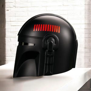 May include: A black helmet with a visor and a red rectangular design on top. The helmet has a smooth, matte finish and a detailed, angular design. The helmet is likely a prop or collectible.