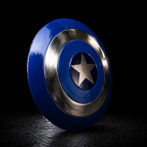 Op de afbeelding: Een blauw en zilver schild met een centrale zilveren ster. Het schild heeft een cirkelvormig ontwerp met een blauw centrum, een zilveren ring en een blauwe buitenrand. Het schild staat tegen een zwarte achtergrond.