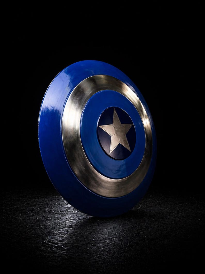 Op de afbeelding: Een blauw en zilver schild met een centrale zilveren ster. Het schild heeft een cirkelvormig ontwerp met een blauw centrum, een zilveren ring en een blauwe buitenrand. Het schild staat tegen een zwarte achtergrond.