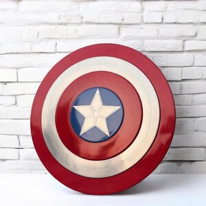 May include: A red, white, and blue Captain America shield. The shield has a red outer ring, a white inner ring, and a silver ring in the middle. The center features a blue circle with a white star. The shield is a prop or collectible.
