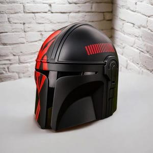 May include: Black helmet with red detailing, including a visor and side features. The helmet has red stripes and a series of red lines on the top. The design is similar to a Mandalorian helmet.