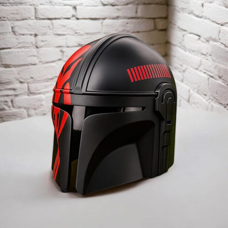 May include: Black helmet with red detailing, including a visor and side features. The helmet has red stripes and a series of red lines on the top. The design is similar to a Mandalorian helmet.