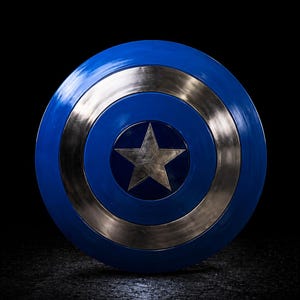 Op de afbeelding: Een blauw en zilver schild met een ster in het midden. Het schild is rond met een blauwe buitenring, een zilveren binnenring en een zilveren ster in het midden. De achtergrond is zwart.