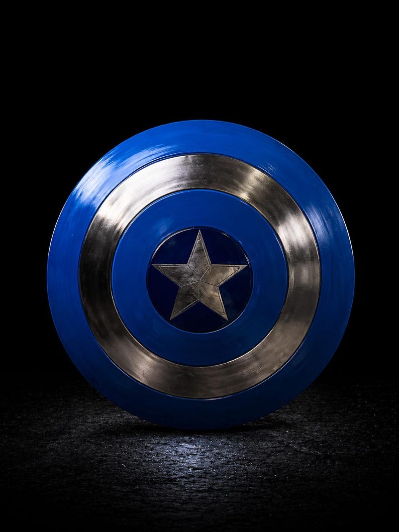 Op de afbeelding: Een blauw en zilver schild met een ster in het midden. Het schild is rond met een blauwe buitenring, een zilveren binnenring en een zilveren ster in het midden. De achtergrond is zwart.