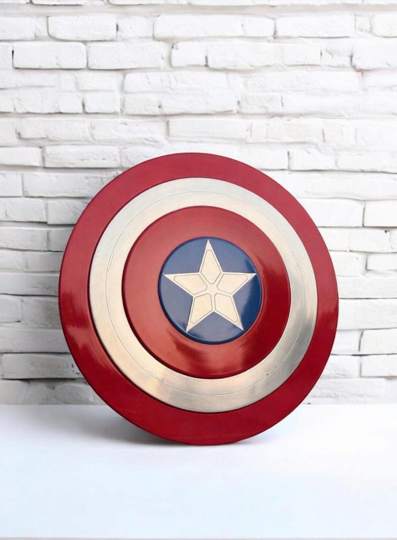 May include: A red, white, and blue Captain America shield. The shield is round with concentric circles of red, silver, and white. A blue circle in the center features a white star. The shield is a popular superhero accessory.