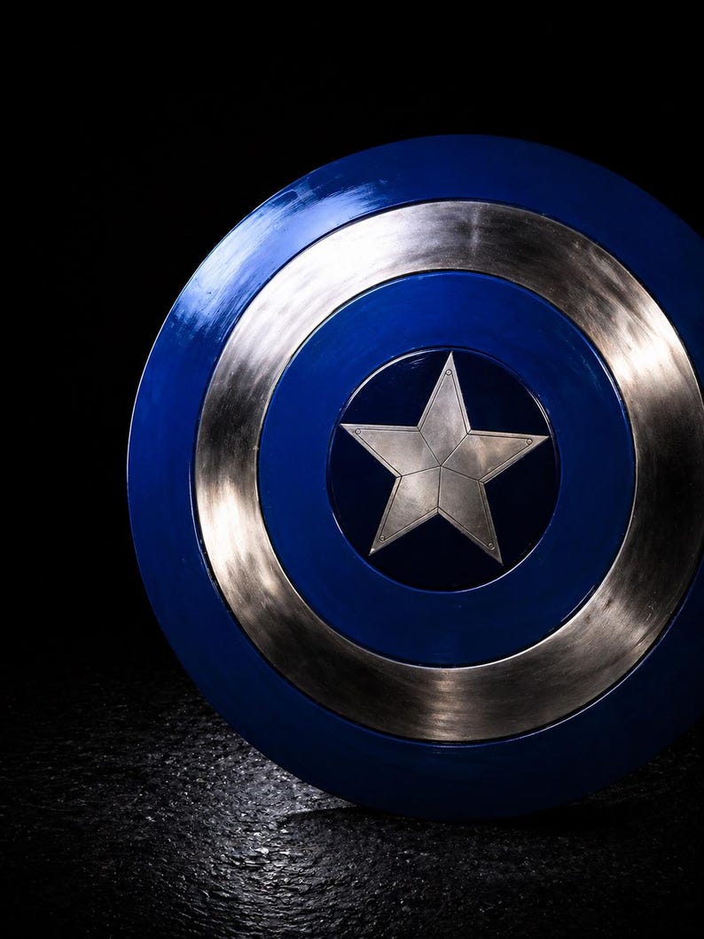 Op de afbeelding: Een blauw en zilver schild met een zilveren ster in het midden. Het schild heeft een cirkelvormig ontwerp met concentrische ringen in blauw en zilver. De ster staat in het midden van het schild. Dit is een rekwisiet of verzamelobject.