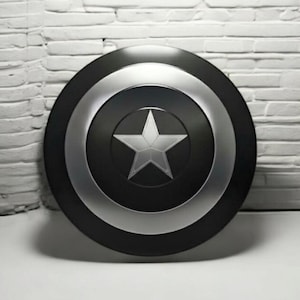 May include: A black and silver shield with a white star in the center. The shield has a circular design with a black center, a silver ring, and a black outer edge. The background is a white brick wall.