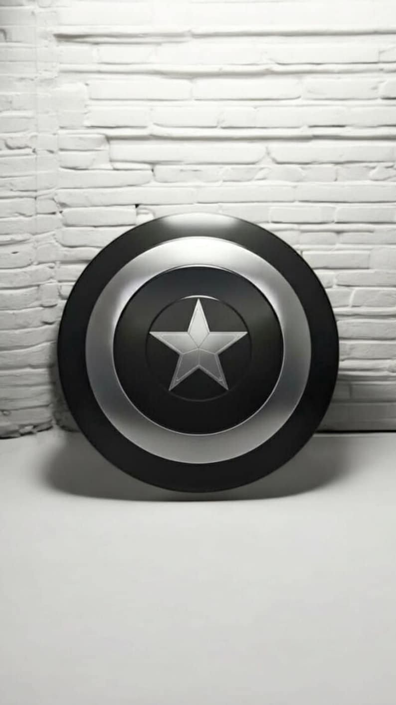 May include: A black and silver shield with a white star in the center. The shield has a circular design with a black center, a silver ring, and a black outer edge. The background is a white brick wall.