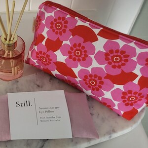 May include: A pink aromatherapy eye pillow with a white label that reads "Still. Aromatherapy Eye Pillow With lavender from Western Australia." A pink floral cosmetic bag and a pink glass diffuser with reeds are also in the image.