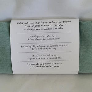 May include: A rectangular, light green eye pillow with a white label wrapped around it. The label contains text about the pillow's filling and use. The pillow is filled with Australian linseed and lavender flowers.