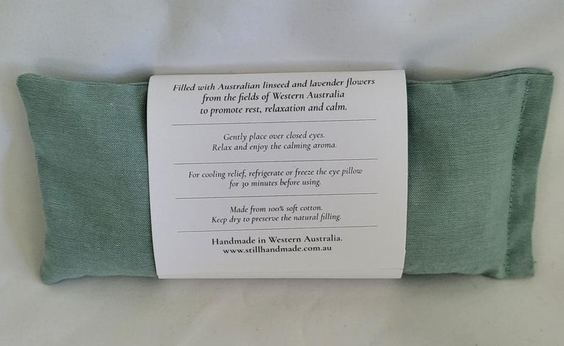 May include: A rectangular, light green eye pillow with a white label wrapped around it. The label contains text about the pillow's filling and use. The pillow is filled with Australian linseed and lavender flowers.