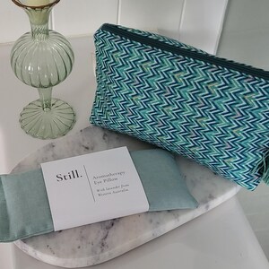 May include: A teal and white chevron patterned cosmetic bag with a green tassel and a decorative gem. An aromatherapy eye pillow and a decorative glass vase are also present. The eye pillow is labeled "Still. Aromatherapy Eye Pillow".