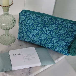May include: A teal cosmetic bag with a leaf pattern, a matching tassel, and a white beaded zipper pull. An aromatherapy eye pillow and a decorative glass candle holder are also present.