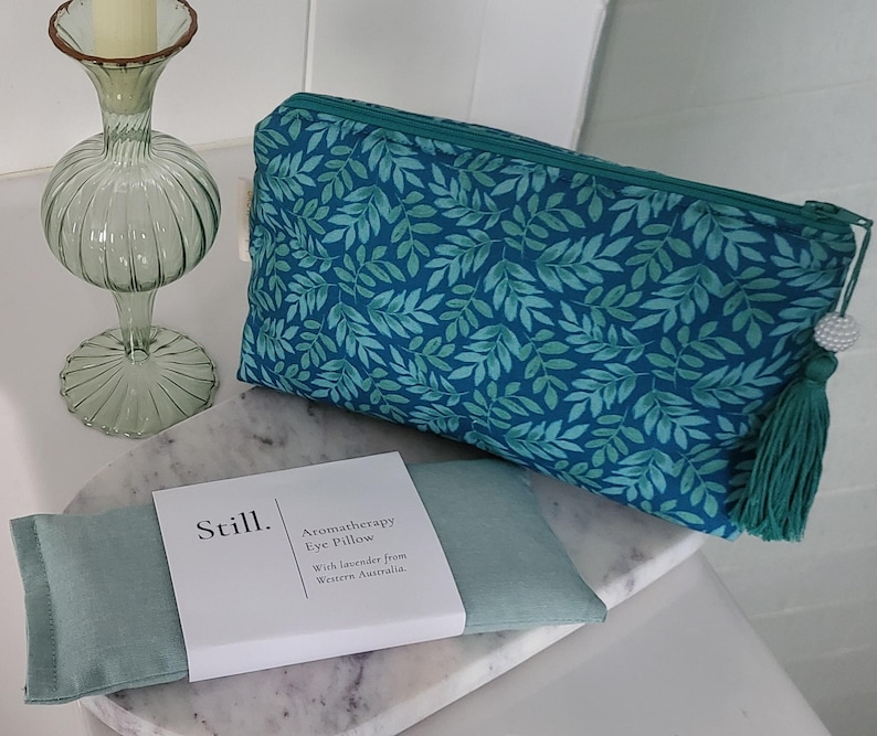 May include: A teal cosmetic bag with a leaf pattern, a matching tassel, and a white beaded zipper pull. An aromatherapy eye pillow and a decorative glass candle holder are also present.