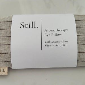 May include: A rectangular aromatherapy eye pillow with a striped pattern in shades of gray and brown. The pillow is labeled "Still" and includes text indicating it contains lavender from Western Australia.