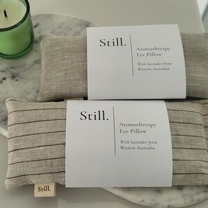 May include: Two aromatherapy eye pillows with the word "Still" on the label. The pillows are beige with dark stripes and are labeled "Aromatherapy Eye Pillow With lavender from Western Australia."