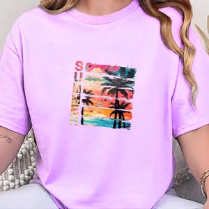 Peut inclure: Un t-shirt violet clair avec un motif estival coloré. Le motif comprend des palmiers, un coucher de soleil et le mot "SUMMER" en texte vertical. Le motif est imprimé sur le devant du t-shirt.
