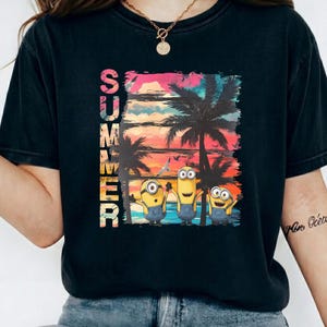 Peut inclure: T-shirt noir avec un graphisme coloré. Le mot "SUMMER" est imprimé verticalement à gauche. Le graphisme représente un coucher de soleil tropical avec des palmiers et trois personnages des Minions sur une plage. Vêtement décontracté.