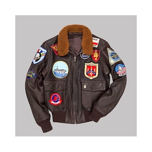 May include: A brown leather bomber jacket with a shearling collar and multiple embroidered patches. The jacket features two front pockets, a zipper closure, and ribbed cuffs. Patches include military and aviation-themed designs.