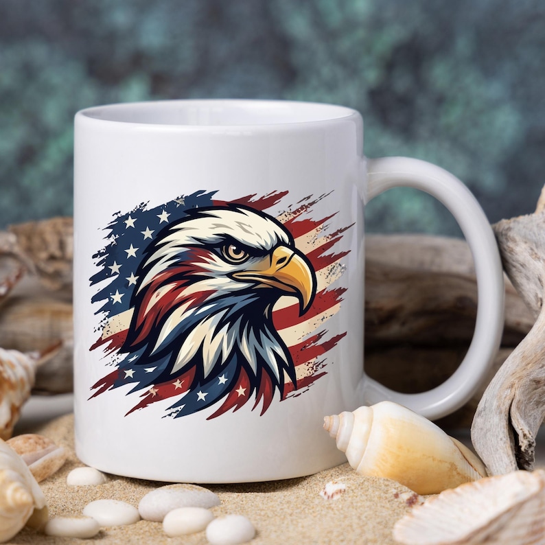 Może przedstawiać: Biały ceramiczny kubek z motywem głowy amerykańskiego bielika. Ilustracja wykorzystuje kolory amerykańskiej flagi: czerwony, biały i niebieski. Głowa orła umieszczona jest na tle pas&oacute;w i gwiazd flagi.