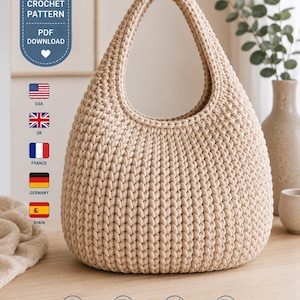 Op de afbeelding: Een beige gehaakte handtas met een afgerond silhouet en een enkel geïntegreerd handvat. De tekst CROCHET PATTERN PDF DOWNLOAD is zichtbaar, samen met iconen voor de VS, VK, Frankrijk, Duitsland en Spanje. De onderste iconen geven INSTANT DOWNLOAD, SAVE FOREVER, EASY TO FOLLOW en PDF PATTERN aan.