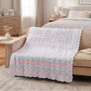 May include: A crocheted blanket featuring a repeating pattern of soft pastel colors including light pink, mint green, and lavender. The blanket has a scalloped edge and a textured, open-weave design that drapes across the surface of a tan sofa.